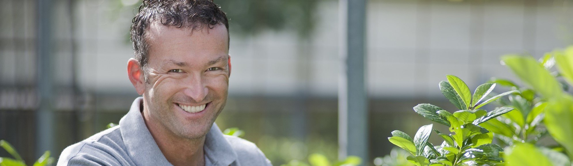 Man aan het werk in de groenvoorziening, glimlachend terwijl hij planten snoeit.