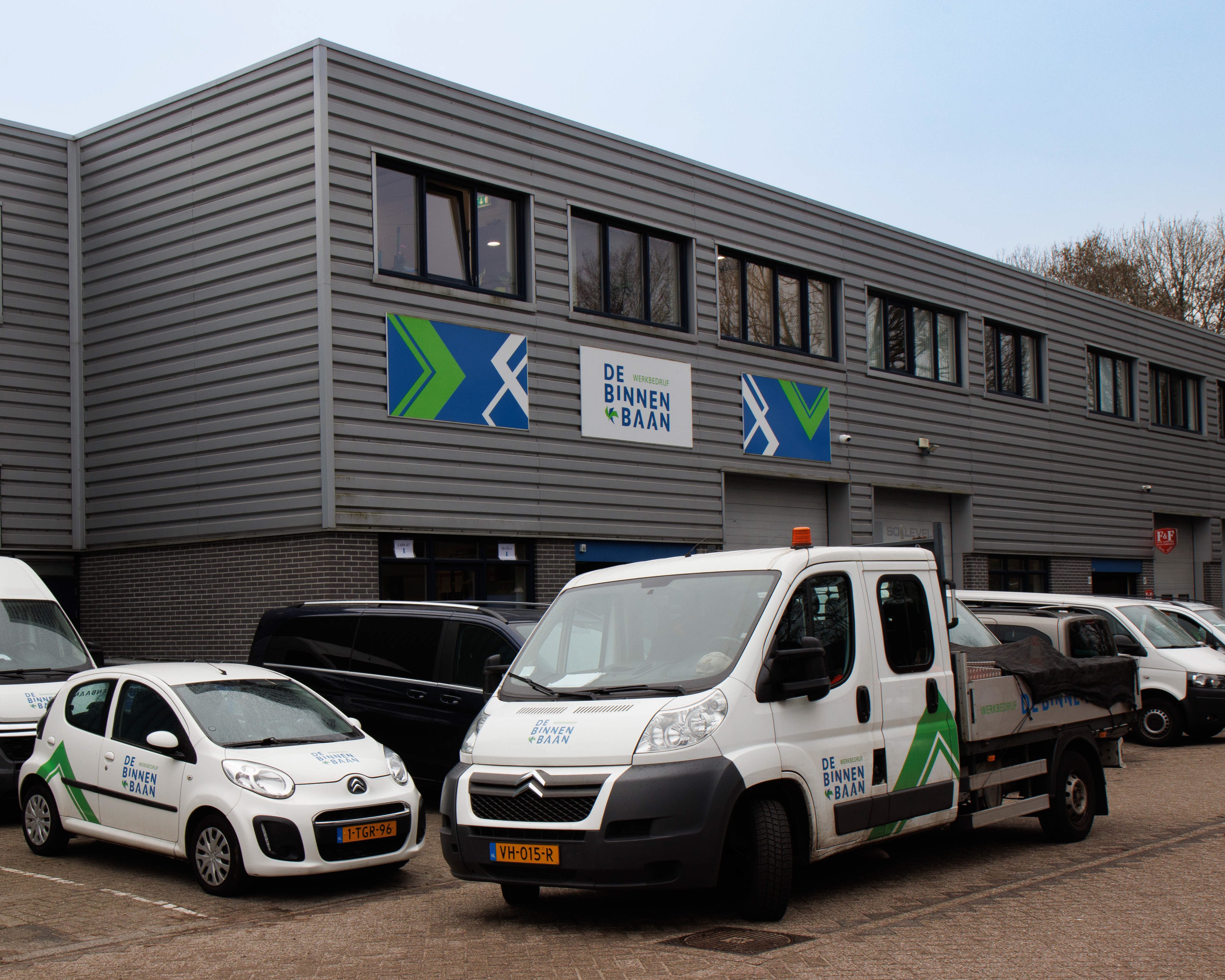Kantoor van De Binnenbaan in Voorburg, met ingang, bedrijfsauto's en bedrijfslogo zichtbaar aan de gevel.