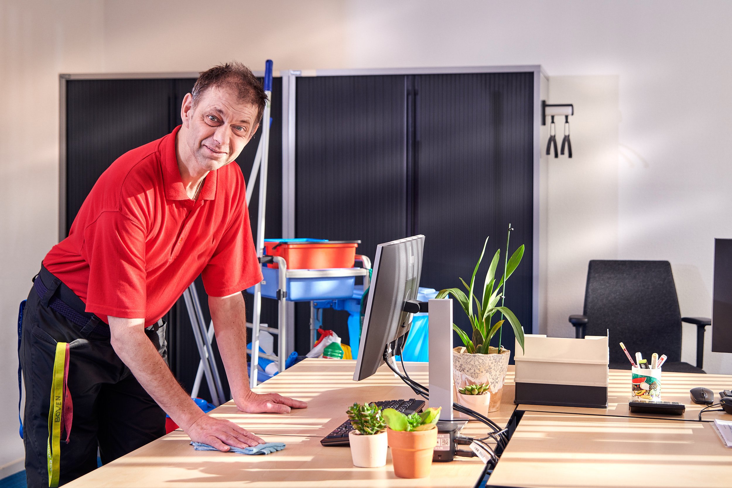Medewerker van De Binnenbaan maakt een bureau schoon in een kantoorruimte als onderdeel van facilitair werk.