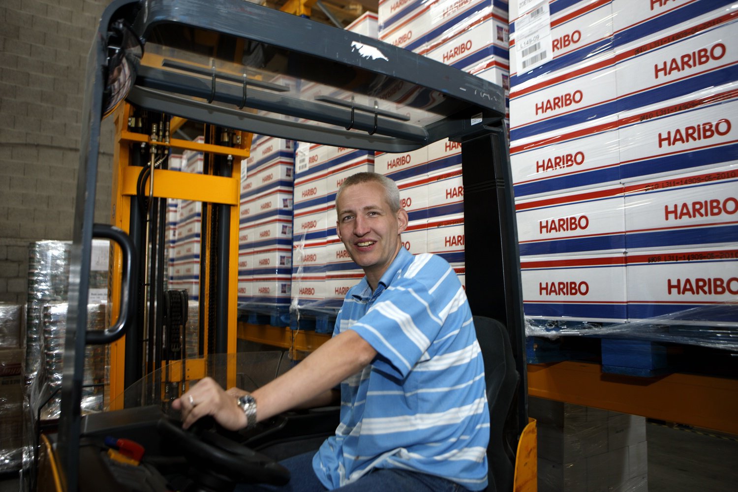 Medewerker bestuurt een heftruck in een magazijn met pallets vol Haribo-dozen.
