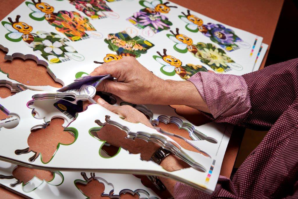Handen drukken kartonnen stickers met kleurrijke bloemenfiguren uit als onderdeel van verpak- en ompakwerkzaamheden bij De Binnenbaan.