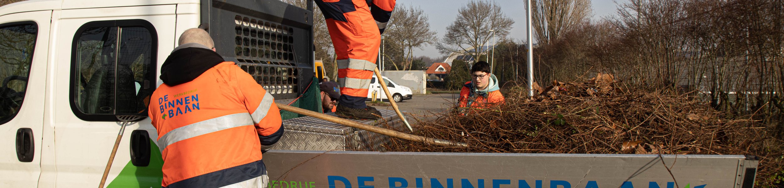 Medewerkers van de Groenacademie van De Binnenbaan voeren groenonderhoud uit en laden snoeiafval in een bedrijfswagen.